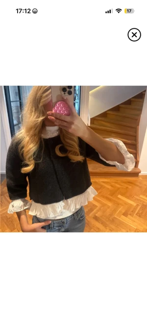 Svart bolerotopp med volangdetaljer - Säljer en svart bolerotopp med vita volangdetaljer vid ärmslut och nederkant. Toppen har en croppad passform och trekvartsärmar, vilket ger en cool och trendig look. Perfekt att styla med jeans eller kjol för en chic vibe.