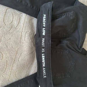 Svarta Peachy Low skinny jeans XS - Svarta skinny jeans från Peachy Low med låg midja och ankellängd. Klassisk femficksdesign, smal passform och stretchigt material som sitter tajt hela vägen ner. Perfekta om du gillar en slimmad siluett och svart vibe.