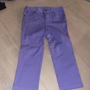 Lila chinos från Polo Ralph Lauren - Snygga oanvända barn byxor i lila från chinos från Polo Ralph Lauren med klassisk rak passform och grönt broderat logomärke på bakfickan. Byxorna har fem fickor, knappstängning och är tillverkade i mjuk bumull. Byxornas storlek är för 5 åringa barn.