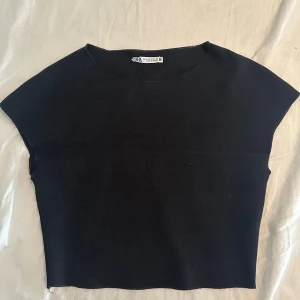 Svart ärmlös topp från Zara - Minimalistisk svart topp från Zara i storlek M. Modellen är ärmlös med breda axlar och har en rak, croppad passform. Materialet är mjukt och stretchigt, perfekt för en clean look. Rund halsringning och slät yta utan detaljer eller mönster.
