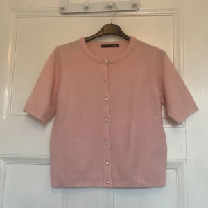 Rosa kofta med pärlknappar - Söt ljusrosa kofta från Lager 157 med korta ärmar och rund halsringning. Koftan är stickad och har pärlknappar framtill som ger en extra gullig touch. 