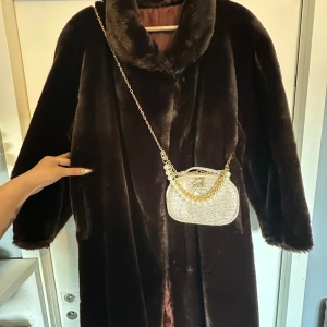 Vintage Fur long Jacket  - Säljer en lång, mörkbrun pälsjacka med bred krage och mjukt foder. Jackan har en klassisk, rak passform och är perfekt för kalla dagar. Den är riktigt fluffig och har långa ärmar med diskreta muddar. Perfekt statement-plagg för dig som vill sticka ut.