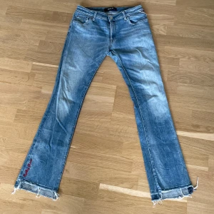 Blå bootcut jeans från Replay - Snygga blå jeans från Replay med bootcut passform och slitna detaljer vid bensluten. Broderad Replay Jeans-text i rött på benet och klassiska fem fickor. Jeansen har en normal midja och är gjorda i jeansmaterial.