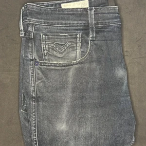 Replay Anbass jeans - Snygga svarta Replay Anbass jeans med diskret tvättad look och klassiska fem fickor. Jeansen har smal passform och är tillverkade i stretchig bomullsdenim för extra komfort. Perfekta för dig som gillar en stilren och modern vibe. Storlek 31/32