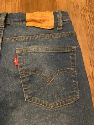 Levi's 514 blå jeans straight fit - Säljer ett par klassiska Levi's 514 jeans i blå denim med regular straight fit och snygga slitningar. Byxorna har fem fickor, orange kontrastsömmar och Levi's röda logotag på bakfickan. Passar dig som gillar tidlös stil och bekväma jeans.