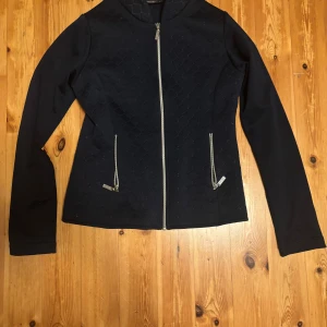 Equestrian stockholm ridjacka - Ridtröja/jacka från equestrian stockholm. Next Generation Jacket i navy är en stilren och fin ridtröja. Lite sliten vid smycket på dragkedjan vid fickorna. Den är välanvänd men ändå i fint skick