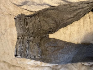 Grå straight jeans med tvättad look - Snygga grå jeans med tvättad finish och klassisk femficksdesign. Modellen har rak passform och normal midja, vilket ger en chill och tidlös vibe. Jeansen är tillverkade i denim och har knappar och dragkedja framtill.