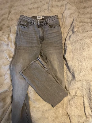 Grå jeans utsvängda jeans med slit från 157 - Snygga grå jeans från 157 med klassisk femficksdesign och raka ben. Jeansen har hög midja och är tillverkade i mjukt denimtyg som ger en skön känsla. Perfekt för dig som gillar en clean och enkel look.