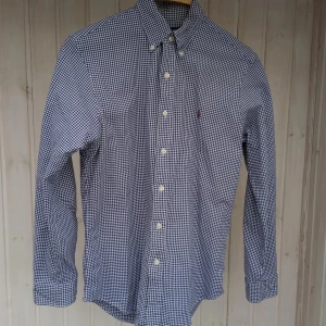 Rutig blåvit skjorta Polo Ralph Laurent - Snygg blåvit rutig skjorta från Polo Ralph Lauren i slim fit-modell. Skjortan har klassisk krage, knappar framtill och långa ärmar. Tillverkad i stretchig bomull för extra komfort. Perfekt för dig som gillar stilren och tidlös look. blå/ vit rutig.