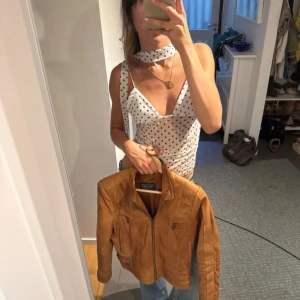 Brun skinnjacka med bälten från Rotary - Säljer en snygg brun skinnjacka från Rotary med coola detaljer som dubbla bälten i midjan och dragkedjor på fickorna. Jackan har en klassisk krage och figurnära passform, perfekt att slänga över en skjorta eller t-shirt. Passar dig som gillar en tidlös men edgy stil.