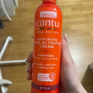 Cantu Curl Activator Cream 355ml - Fuktgivande curl activator cream från Cantu med sheasmör, perfekt för naturliga lockar, coils och vågor. Ger glans, definierar och mjukgör håret. Kommer i en orange plastflaska med vitamin B-komplex och fair trade sheasmör.