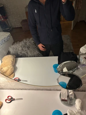 Mörkblå hoodie från Polo Ralph Lauren - Säljer en mörkblå hoodie från Polo Ralph Lauren med vit logga på bröstet. Tröjan har huva med snörning, dragkedja framtill och en stor ficka på magen. Perfekt för dig som gillar stilren och enkel streetwear.