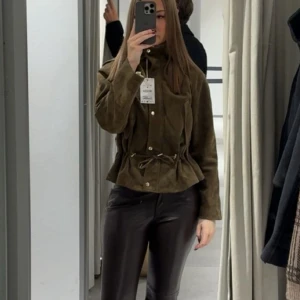 Brun mockajacka med huva och snörning - Säljer en brun jacka från Zara med mockaeffekt, huva och snygg snörning i midjan. Nyskick. Jackan har långa ärmar, stora fickor och knappar framtill. Perfekt för dig som gillar en loose fit och vill ha en cool look