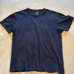 Mörkblå t-shirt från Polo Ralph Lauren - Snygg mörkblå t-shirt från Polo Ralph Lauren med klassisk röd logobrodyr på bröstet. Modellen har rund hals och korta ärmar. Tillverkad i mjuk bomull som känns skön mot huden. Perfekt för dig som gillar stilrena och tidlösa plagg. Priset går att diskuteras vid snabbaffär!