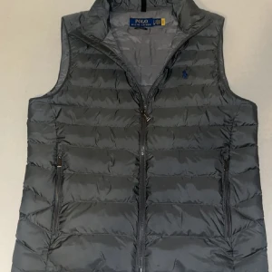  Polo Ralph Lauren-dunväst - ✍🏼 Storlek S men passar även M 🖤 Grå & stilren 🪶 Lätt & smidig – perfekt lagerplagg 🧥 Hög krage – värme utan bulk 💯 Knappast använd – toppskick 🗽 Köpt i NY direkt från Polo Ralph Lauren butiken 🔗 QR-kod finns på plagget – kan skannas för att autentisera på Ralph Laurens hemsida  💸 Riktigt kap! Liknande västar: 3 000–4 000 kr i butik  🔥 Fynda nu – först till kvarn! 💌 Skicka meddelande direkt!