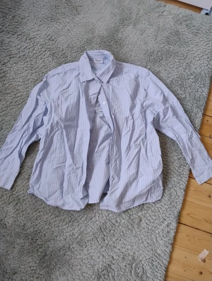 Blåvit randig skjorta från Kappahl - Snygg skjorta från Kappahl i ljusblått med vita ränder. Klassisk krage och knappar framtill, långärmad och tillverkad i mjuk bomull. Knappt använd.