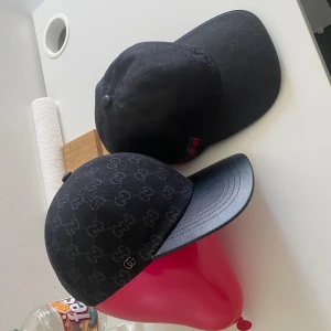 Svart Gucci keps med GG-mönster - Säljer en svart keps från Gucci med klassiskt GG-monogram över hela kepsen. Kepsen har böjd skärm, justerbar rem bak och en liten metallogo på sidan. Materialet är bomull och detaljerna är i svart. Perfekt för dig som vill ha en stilren och lyxig accessoar.