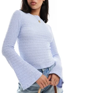 Ljuslila långärmad topp med utsvängda ärmar - Supersöt ljuslila långärmad topp med vågigt stickat mönster och breda utsvängda ärmar. Sitter figurnära över kroppen och har en mjuk, stretchig känsla. Perfekt att styla med jeans eller kjol för en trendig look.