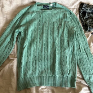 Grön kabelstickad tröja Gant - Snygg ljusgrön kabelstickad tröja från Gant med rund halsringning och diskret logga på bröstet. Tröjan har långa ärmar och ribbade muddar vid ärmslut och nederkant. Perfekt för lager-på-lager under kyliga dagar. Ny pris 1900kr