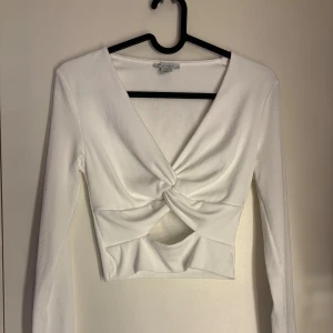 Vit topp från Amisu - Säljer en vit ribbad topp från Amisu i omlottmodell med twistad detalj framtill i storlek S.