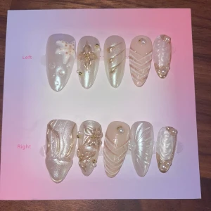 S - pärlemor press-on naglar - Snygga press-on naglar i pärlemorvitt och nude med guldiga detaljer, pärlor och 3D-mönster. Mix av spetsiga och fyrkantiga former, dekorerade med stjärndetaljer och skimrande effekter. Perfekt för dig som vill ha unika och trendiga naglar utan salongsbesök.