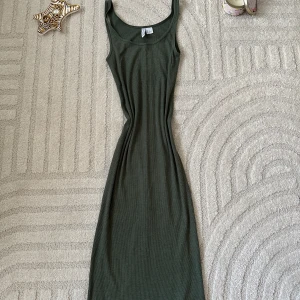 Mörkgrön ribbad långklänning - Snygg mörkgrön långklänning med ärmlös design och rundad halsringning. Klänningen är ribbad och har en tight passform som framhäver figuren. Perfekt för dig som gillar en enkel men stilren look.