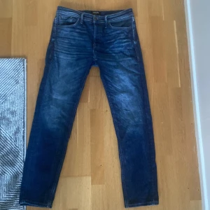Blå jeans från Jack & Jones, 32/32 - Snygga blå jeans från Jack & Jones i klassisk femficksmodell. Jeansen har en rak passform och är tillverkade i slitstarkt denimtyg. Perfekta för dig som gillar en tidlös look med lite tvättade detaljer och normal midja.