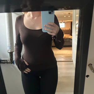 Brun långärmad topp med rund hals - Säljer en brun långärmad topp med rund, djup urringning. Modellen är tight och sitter snyggt mot kroppen. Perfekt att styla med jeans eller kjol för en enkel men stilren look.🩷