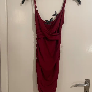 Vinröd tight klänning från Shein XS - Säljer en vinröd kort klänning från Shein i storlek XS. Klänningen har smala axelband, draperad framsida och rynkade detaljer längs sidorna och bak. Sitter tight och har en snygg, figurnära passform. Perfekt för dig som vill sticka ut med en djup färg och trendig look.