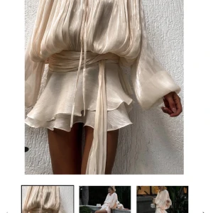 Champagnefärgad omlottklänning med volang - Superfin kort klänning i champagnefärgat, glansigt material med plisserade detaljer. Långa ärmar, omlottknytning i midjan och volangig kjol. Perfekt för dig som gillar en romantisk och trendig look med extra volym och flow.