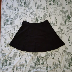 Svart kortkjol från H&M - Svart kortkjol från H&M Divided i storlek L. Kjolen har en lätt utställd form och en synlig dragkedja bak. Tillverkad i mjuk polyester som ger en skön känsla och snygg passform. 