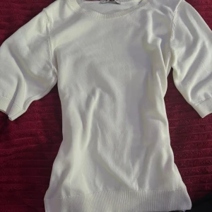 Vit stickad kortärmad tröja - Snygg vit stickad tröja med korta ärmar och rund halsringning. Tröjan har en enkel och clean design med ribbade muddar vid ärmslut och nederkant. Perfekt för lager-på-lager eller som den är under varmare dagar.
