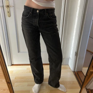 Svarta raka jeans från Zara - Säljer ett par svarta Zara-jeans med klassisk rak passform och medelhög midja. Jeansen har fem fickor, bälteshällor och stängs med knappar. Perfekta för en avslappnad och stilren look.          Jag är 177 cm för referens.                                Säljer då jag inte får användning för dem längre. Skriv gärna vid frågor! ☺️