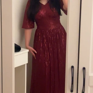 Glittrig vinröd långklänning - Säljer en glittrig vinröd långklänning med v-ringad hals och halvlånga ärmar. Klänningen har ett elegant fall och skimrande detaljer som fångar ljuset. Perfekt för dig som vill sticka ut med en glamorös look.