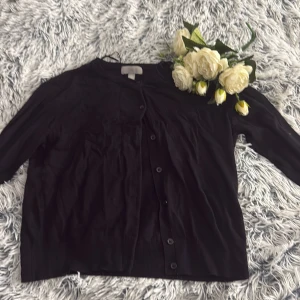 Svart kofta med knappar - En klassisk svart kofta med rund halsringning och knäppning framtill. Koftan har långa ärmar och är tillverkad i ett mjukt material som passar perfekt för lager-på-lager-stil. Enkel och stilren design som funkar till det mesta.