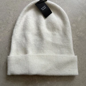 Vit ribbad mössa från Bik Bok - Vit ribbstickad mössa från Bik Bok i mjuk alpackablandning. Klassisk form med uppvikt kant, perfekt för kalla dagar. Materialet består av polyamid, akryl, alpacka, ull och elastan för extra komfort och stretch.