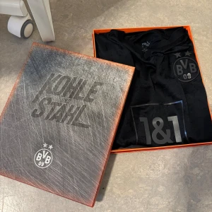 BVB x Puma svart limited edition tröja - Exklusiv svart Borussia Dortmund fotbollströja från Puma med diskret mönster, BVB 09-logga och 1&1 sponsortryck på bröstet. Tröjan har korta ärmar, V-ringning och är tillverkad i ett lätt, tekniskt material. Kommer i specialbox med 'Kohle und Stahl'-tema. Pris kan diskuteras!