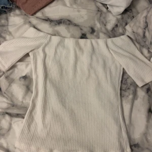Vit ribbad offshoulder topp H&M - Säljer en vit ribbad topp från H&M i storlek S. Modellen är offshoulder med korta ärmar och har en slim passform som sitter snyggt. Perfekt för dig som gillar stilrena och enkla plagg med lite edge.