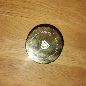 Banana Setting Powder från Bellápierre - Banana Setting Powder från Bellápierre i en rund transparent burk med glansigt guldlock. Pudret är ljusgult och används för att fixera smink och ge en jämn finish. Perfekt för att ljusa upp och korrigera hudtonen. Snygg och praktisk förpackning.