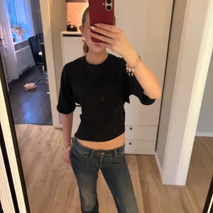 Svart croppad topp med knyt från Nelly - Svart croppad topp från Nelly i bomull med korta ärmar och snygg knytning i ryggen. Enkel och stilren design som passar perfekt till jeans eller kjol. Modellen är rak och lite loose för en avslappnad vibe. I storlek xs.