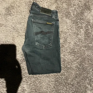 Svarta jeans från Nudie Jeans - Säljer ett par svarta skinny jeans från Nudie Jeans med klassisk femficksdesign och snygga slitningar på bakfickorna. Jeansen har stretchigt denim för extra komfort. 