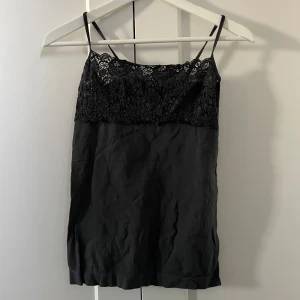 Grå linnetopp med spets - Snygg grått linne med tunna axelband och dekorativ spets upptill. Toppen har en slät nederdel i mjukt tyg och en spets upptill