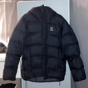 Svart dunjacka/vinterjacka Haglöfs - Säljer en svart dunjacka från Haglöfs i storlek M. Jackan har en schysst puffer-look, huva och dragkedja framtill. Perfekt för kalla dagar och riktigt skön att bära. Klassisk Haglöfs-logga på bröstet och baktill. Snygg och enkel design.