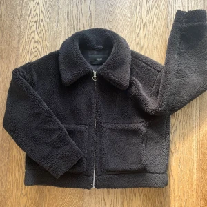 Teddyjacka - Mjuk och fluffig svart teddyjacka från Bik Bok med stor krage och två rejäla framfickor. Jackan har en metallring på dragkedjan och är lite oversized i modellen. 