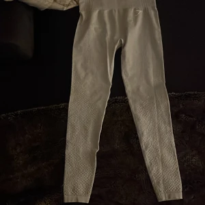 Vita seamless leggings från Gymshark - Säljer ett par vita seamless leggings från Gymshark med hög midja och diskret mönstrad struktur längs benen. De är stretchiga och sitter tight, perfekta för träning eller chill. Materialet är mjukt och följsamt för maximal komfort.