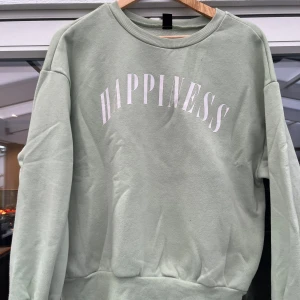 Mintgrön sweatshirt med tryck - Superfräsch mintgrön sweatshirt med texten 'HAPPINESS' i vitt över bröstet. Tröjan har rund halsringning, långa ärmar och ribbade muddar vid ärmslut och nederkant. Perfekt för en chill och avslappnad stil.