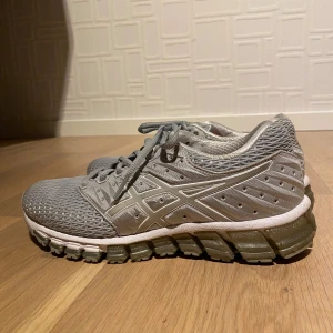 Grå Asics sneakers - Säljer ett par grå Asics Gel-Quantum sneakers med cool mesh-överdel och tydlig Asics-logga på sidorna. Skorna har snörning, dämpad sula och sportig vibe. Perfekta för dig som gillar stilrena och bekväma träningsskor. Pris kan diskuteras!