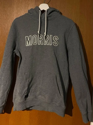 Morris Hoodie - Säljer denna gråa hoddie från Morris. Den är i fint skick och kvalitativt material. Den har vita snören och ”Morris” broderat stort över bröstet. Kom gärna med frågor!