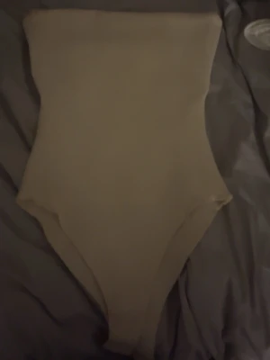 Beige bandeau body från Zara - Säljer en stilren beige bandeau body från Zara i storlek S. Toppen är axelbandslös och har en enkel, tight passform som sitter snyggt mot kroppen. Materialet känns mjukt och stretchigt, perfekt för att skapa en clean look.