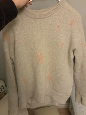 Beige Kashmir  tröja Zadig & Voltaire - Supermysig beige stickad tröja från Zadig & Voltaire med ljusrosa stjärnor som mönster. Tröjan har rund hals, ribbade muddar och lång ärm. Perfekt för att få en chill och snygg look, passar till jeans eller kjol.